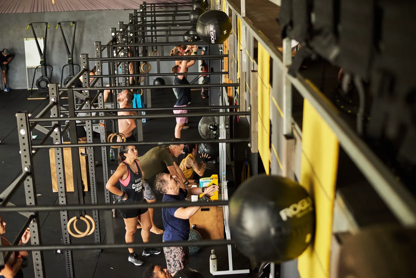Le rig vu dans sa longueur, barres et kettlebells rangées, des membres à l'entraînement au fond.