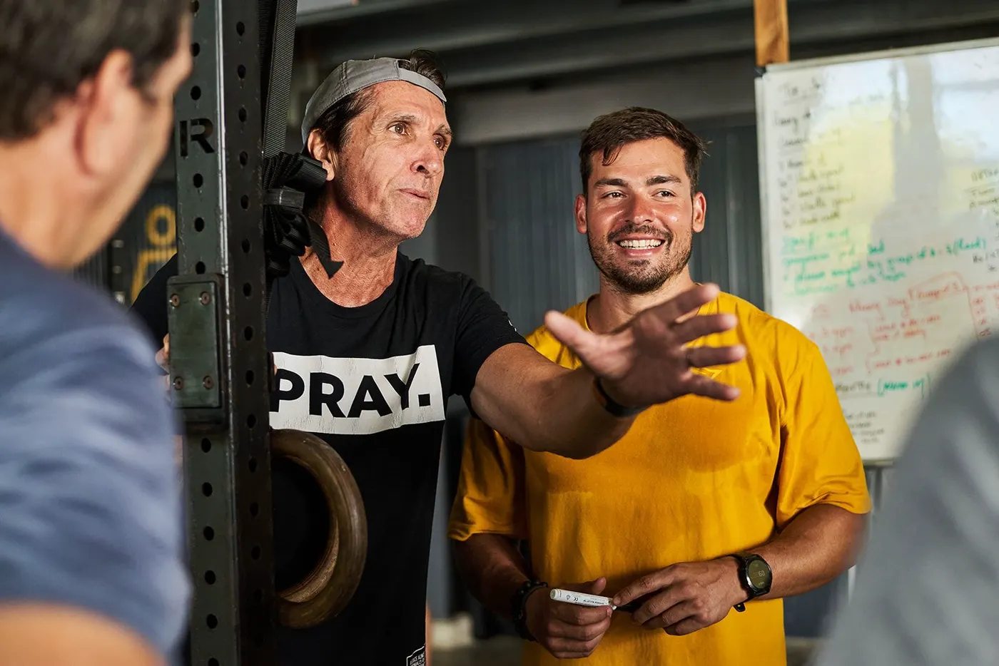 Un coach et un membre en pleine discussion, tous les deux souriants, le tableau blanc derrière eux.
